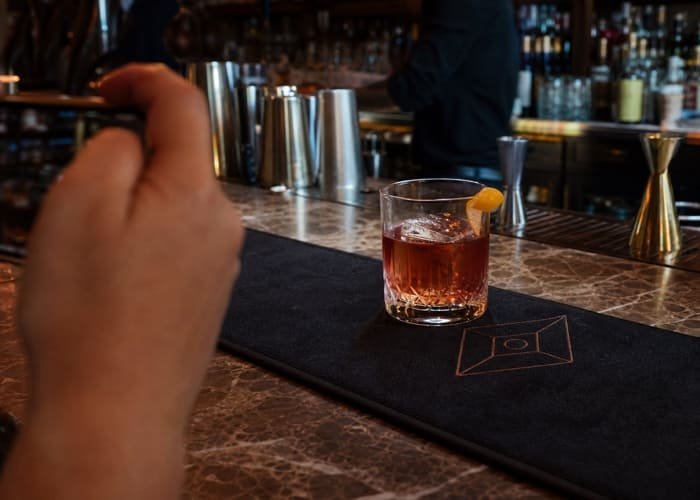 Custom Bar Mat as a Marketing Touchpoint A customer's drink sitting on a branded custom bar mat, with the brand logo clearly visible in the background of the photo.