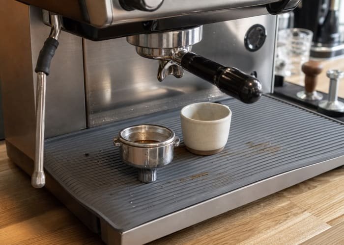 A sleek gray silicone bar mat placed under a professional espresso machine