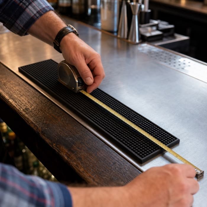 A person using a tape measure on a bar counter to get the correct dimensions for a new bar mat