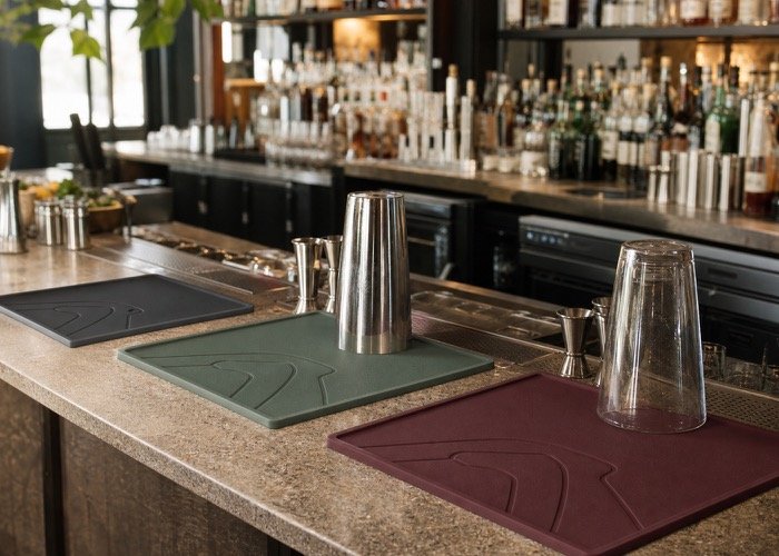 A stylish bar setup featuring custom bar mats in charcoal gray and sage green.