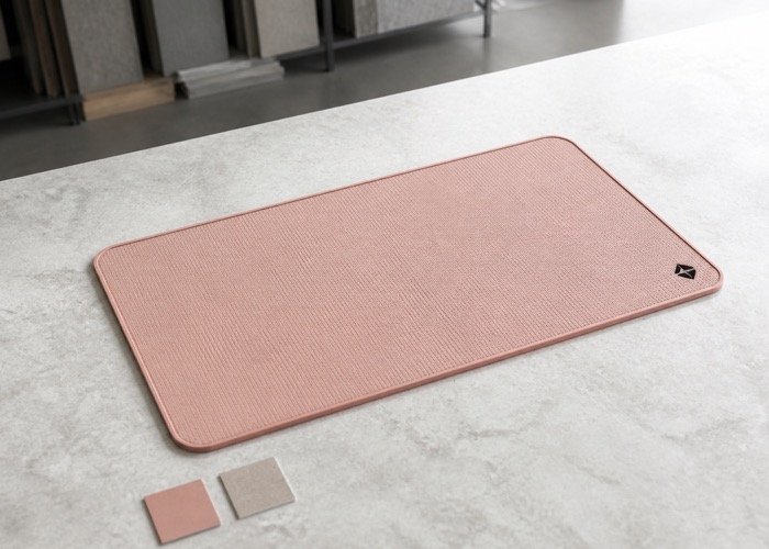 A minimalist custom bar mat in a soft, dusty pink color with a small, simple black logo in the corner